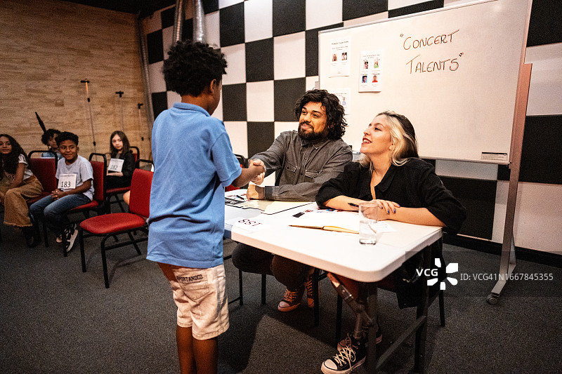 男孩在音乐比赛中与评委握手，包括一位残疾人士图片素材