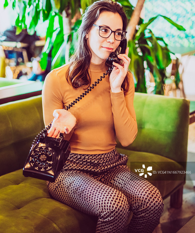 年轻女子在复古客厅使用老式转盘电话图片素材