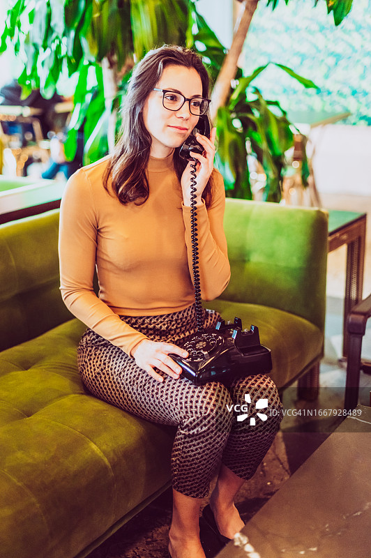 年轻女子在复古客厅使用老式转盘电话图片素材