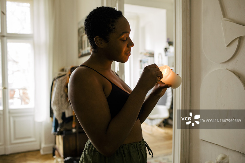 在家手持点燃的蜡烛的微笑年轻女性侧视图图片素材