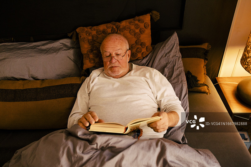 在家躺在床上看书的年长男人图片素材
