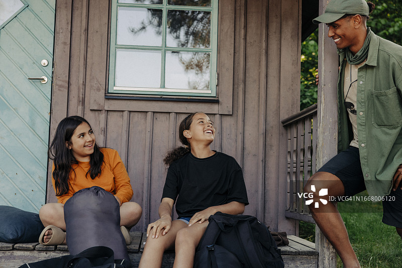 夏令营中坐在小屋旁与男性辅导员交谈的微笑女孩图片素材