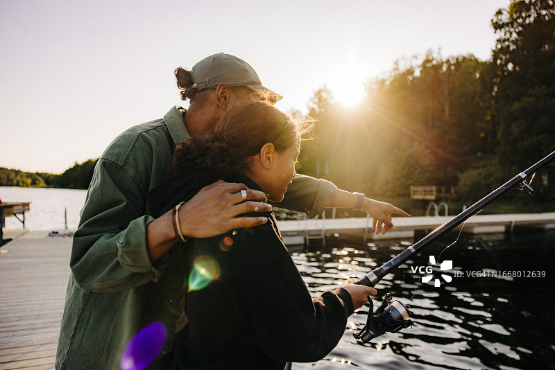 夏令营：男人指导女孩在湖边码头钓鱼图片素材