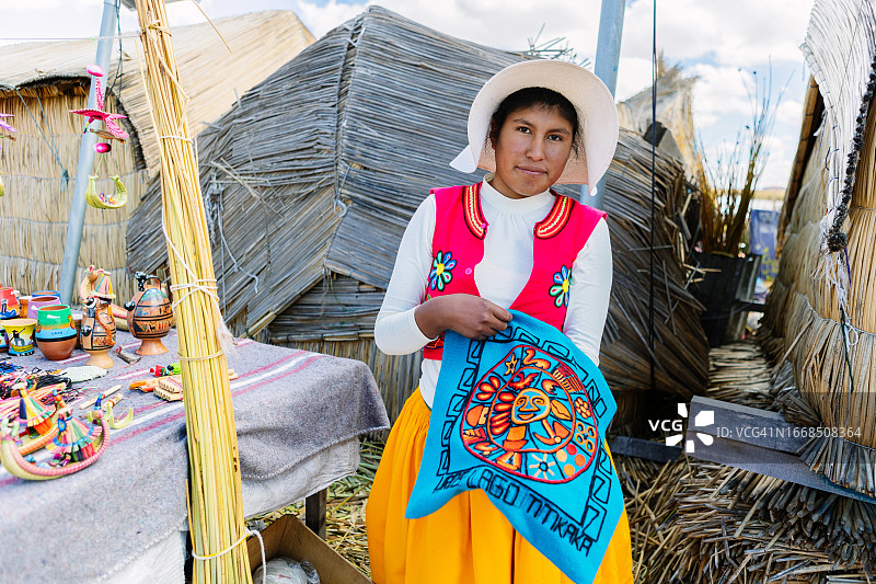 年轻拉丁美洲秘鲁妇女身着传统服装，在的的喀喀湖乌罗漂浮岛上展示手工彩色布料纺织品。艾马拉土著居民。图片素材