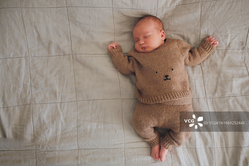 温馨午睡：针织羊毛套装婴儿在亚麻床罩上安详地睡着图片素材