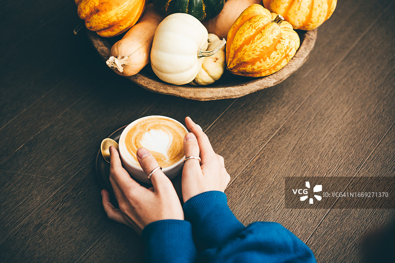 女人手捧咖啡杯。咖啡杯旁有装饰性橙色南瓜，用于秋季装饰。秋季节日图片图片素材