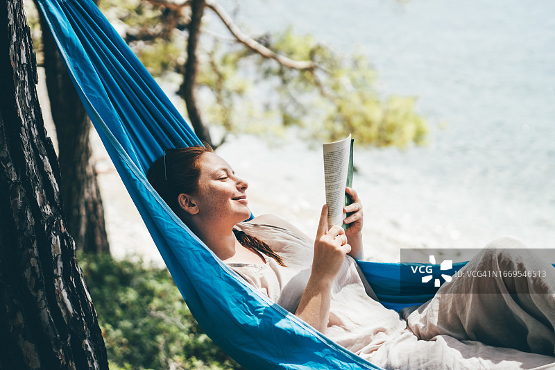 女人在海边森林的吊床上放松读书图片素材