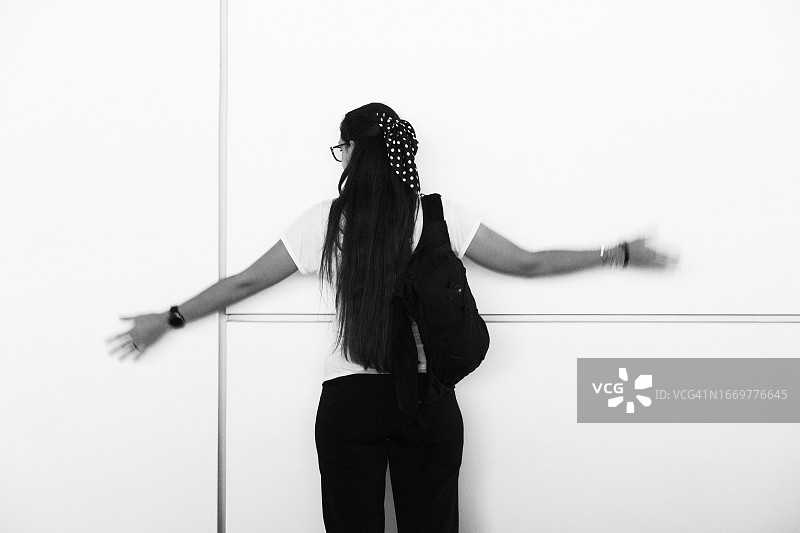 背对着白墙，举起双臂的年轻女子剪影图片素材