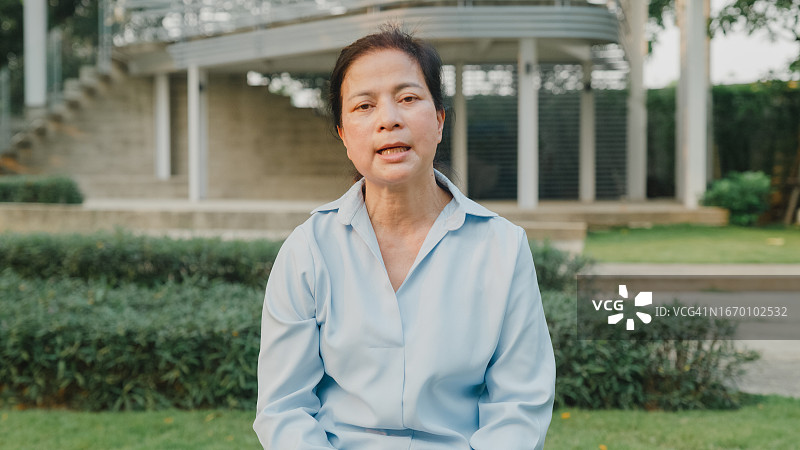 年长的亚洲妇女看着镜头分享在公园里的精神健康体验图片素材
