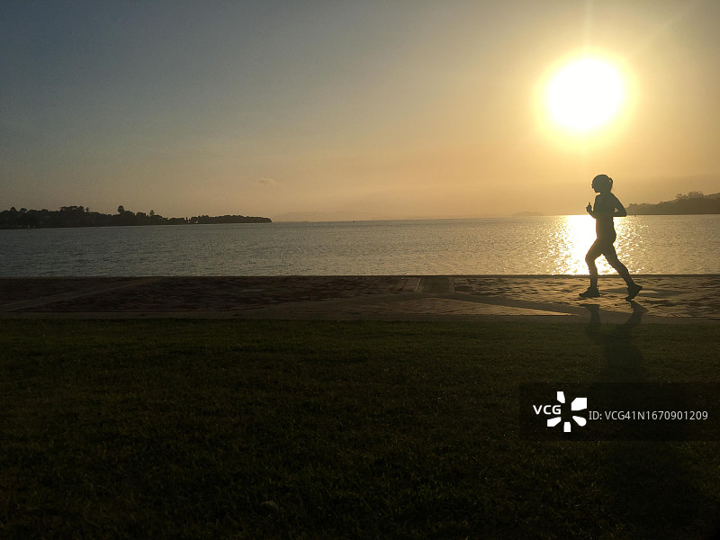 日落时分在海滩上奔跑的成年女子剪影图片素材