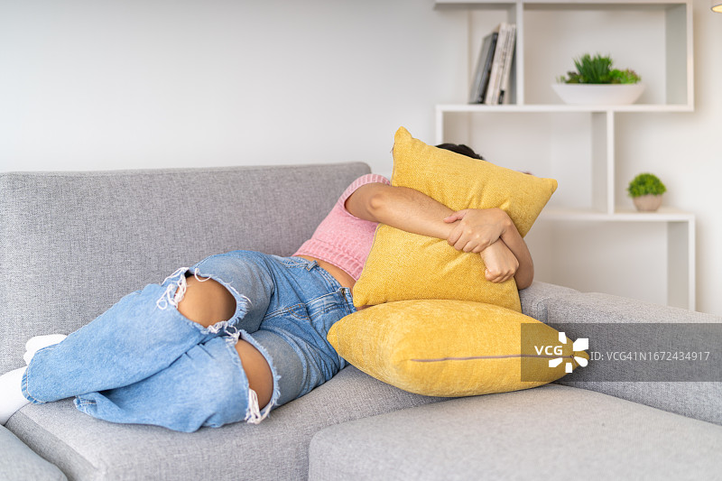 在沙发上用枕头捂住脸的悲伤女人图片素材