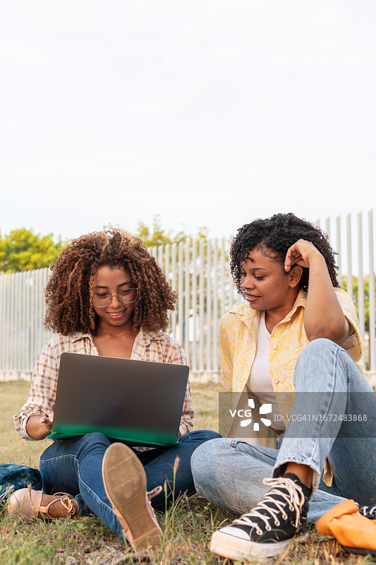 在大学校园草坪上使用笔记本电脑的两个年轻学生图片素材