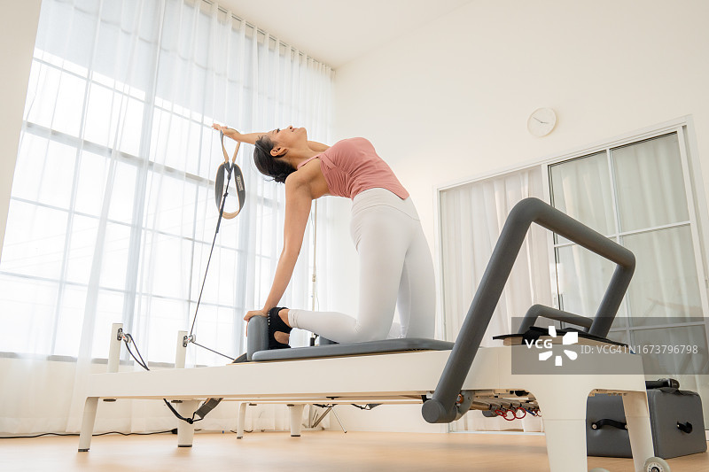 年轻女人在健身俱乐部的普拉提器械上伸展图片素材