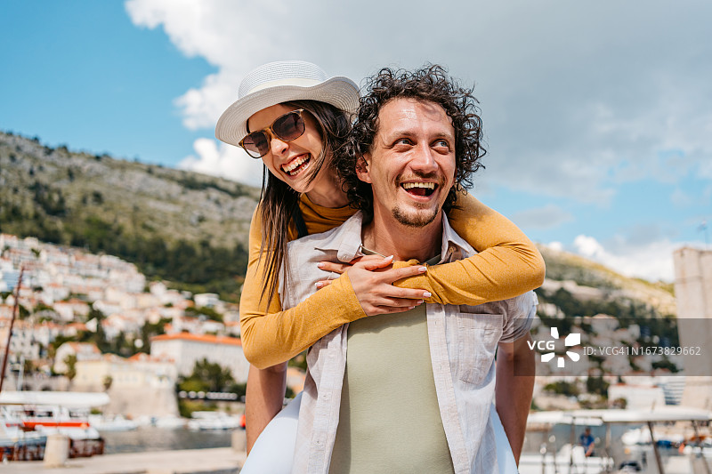 年轻男人在杜布罗夫尼克海湾背着他的女朋友图片素材