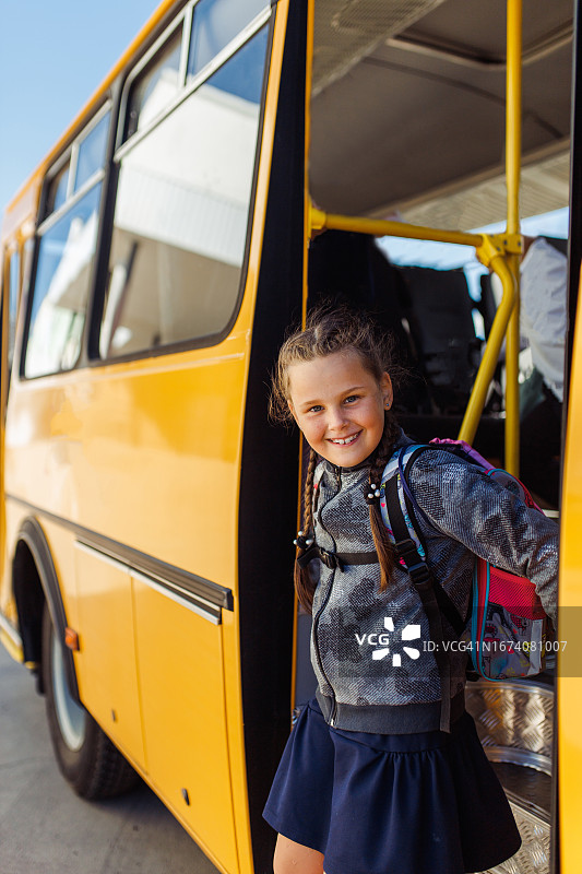 快乐的女小学生背着书包从黄色校车上下来图片素材
