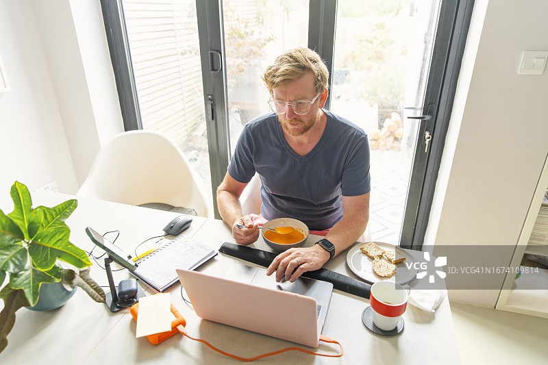 红发中年男人在家工作。他午餐吃的是健康的自制番茄汤图片素材