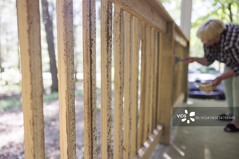 木制门廊真菌预防和防水，中年妇女用含氯保护漆涂抹木栅栏，以防止真菌生长，重点在木栅栏。图片素材