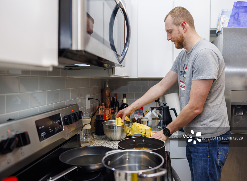 家庭主夫在厨房做饭。成熟的男人在现代厨房里切菠萝，并在锅里煮食物图片素材
