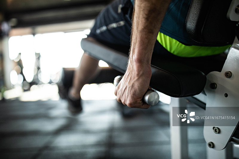 在健身房的机器上锻炼的无法辨认的健壮男人的特写图片素材