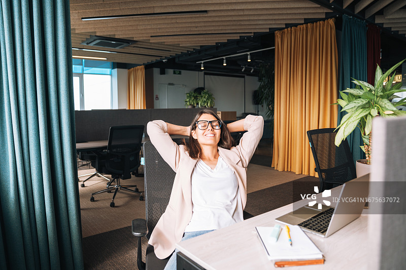 穿米色西装戴眼镜的年轻女人在现代办公室休息图片素材