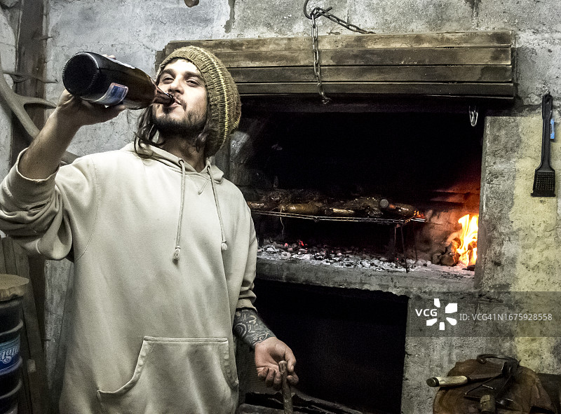 在阿根廷巴里洛切，一个男人一边喝啤酒一边烤肉图片素材