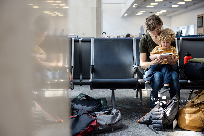 母亲在机场航站楼用智能手机和幼儿互动图片素材