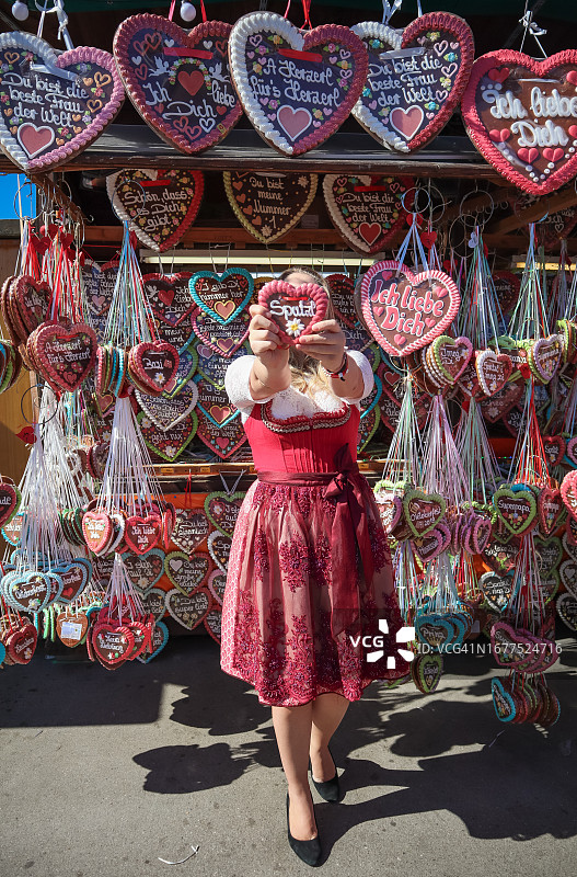 穿着德国传统服装的金发女人在啤酒节上购买姜饼心纪念品图片素材