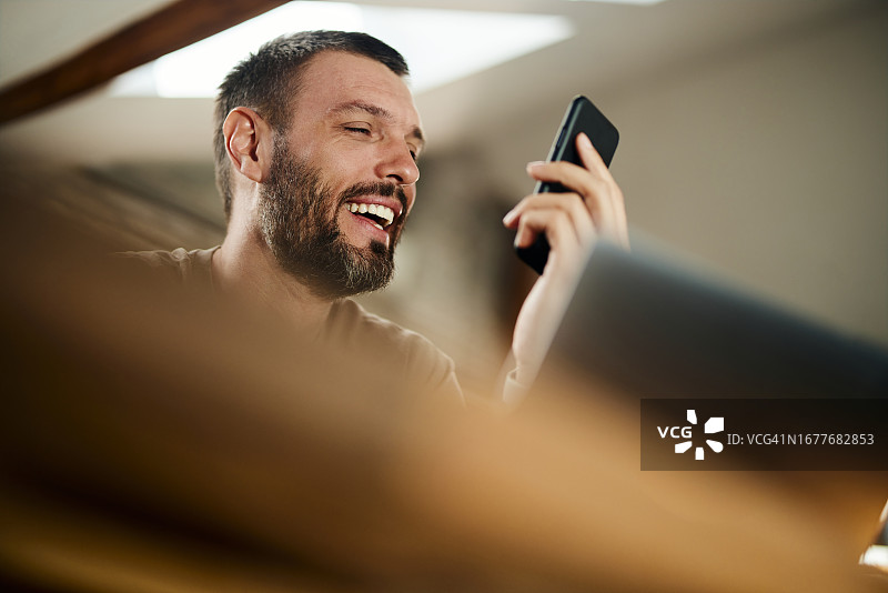 快乐的男人在家工作时使用手机的语音助手图片素材