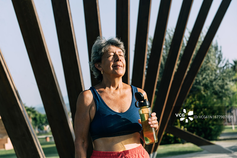 年长的灰发女人公园锻炼后喝水图片素材