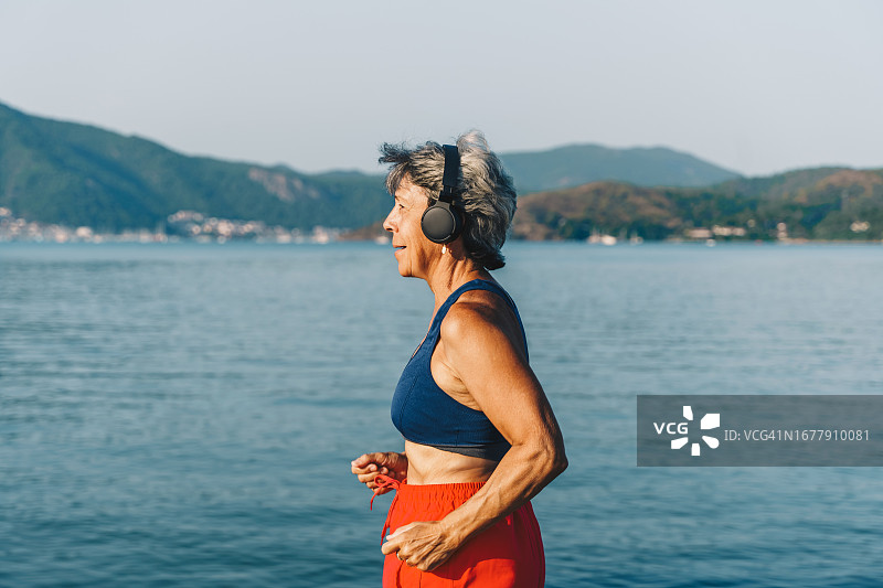 在阳光明媚的夏日，戴着耳机在公园跑步的年长女性图片素材