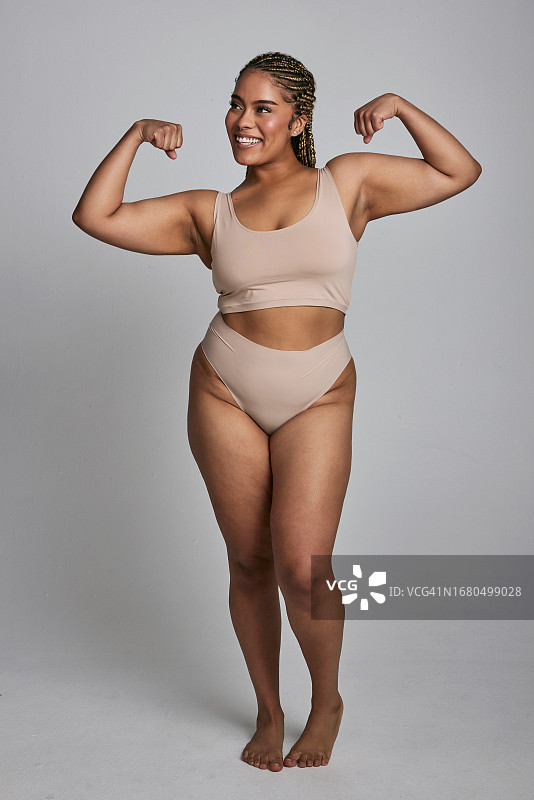 灰色背景上展示自信、曲线美和健康的快乐女性，穿着内衣展示身体自信图片素材