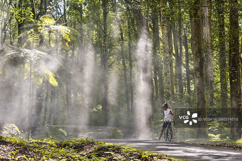 男人在热带森林小路上骑公路自行车休息图片素材