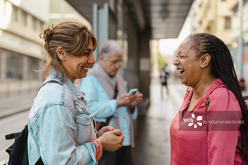 快乐的跨种族女性朋友在公交车站聊天图片素材