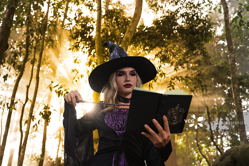 万圣节概念：女巫在森林里祈祷魔法书图片素材