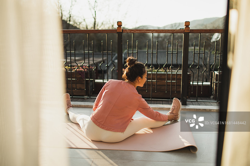 美丽的女人坐在阳台上练习瑜伽。图片素材