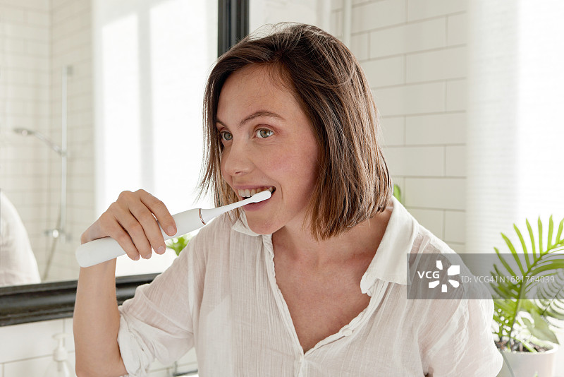 女人在家中浴室用电动牙刷刷牙图片素材
