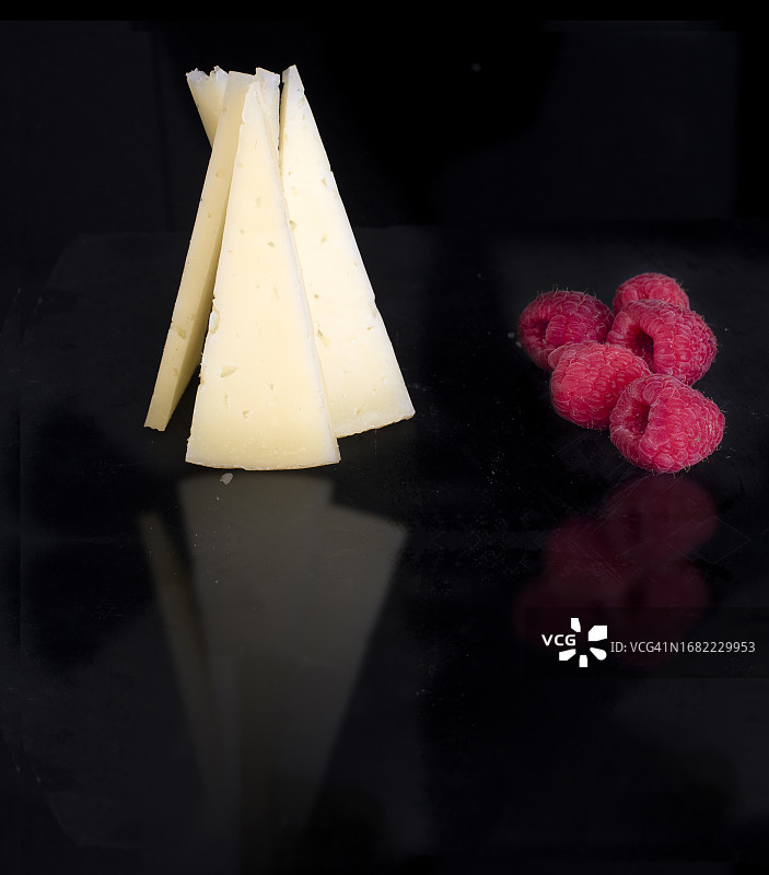 覆盆子装饰的奶酪金字塔，在黑色表面上反射图片素材