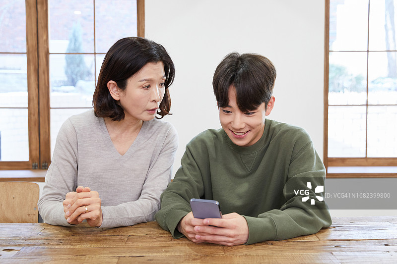 中年妇女、年轻男子、母亲、儿子、智能手机、窥视、微笑图片素材