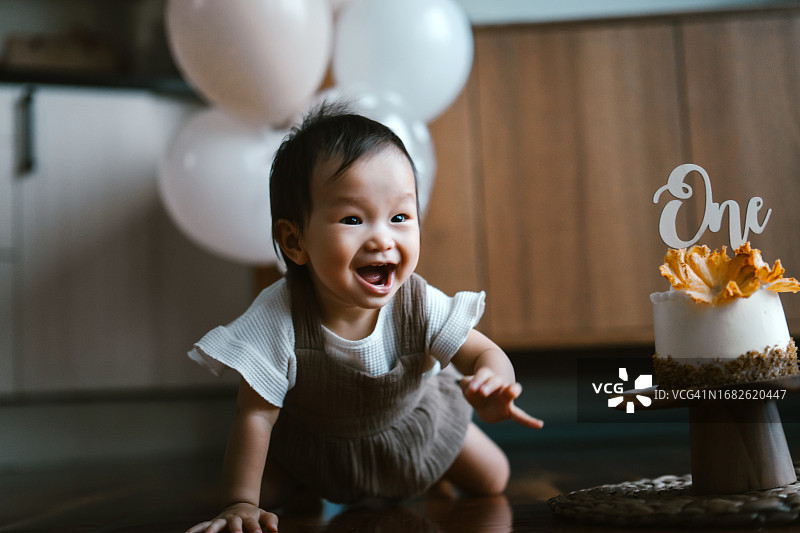 亚洲女宝宝在家庆祝一周岁生日，客厅装饰着气球和生日蛋糕，生日庆祝派对主题图片素材