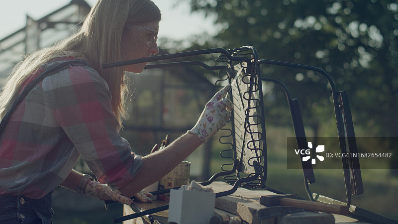 女孩正在花园里翻新旧椅子，在铁锈上涂腻子，DIY项目。图片素材