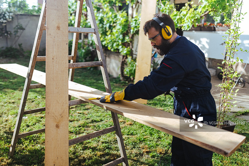 一名工人在院子里用曲线锯切割木板装修房屋图片素材