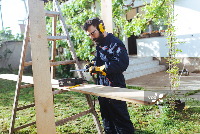 辛勤的蓝领工人在院子里使用曲线锯图片素材