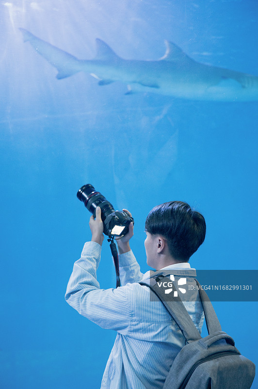 男背包客在水族馆里用相机拍摄海洋生物图片素材