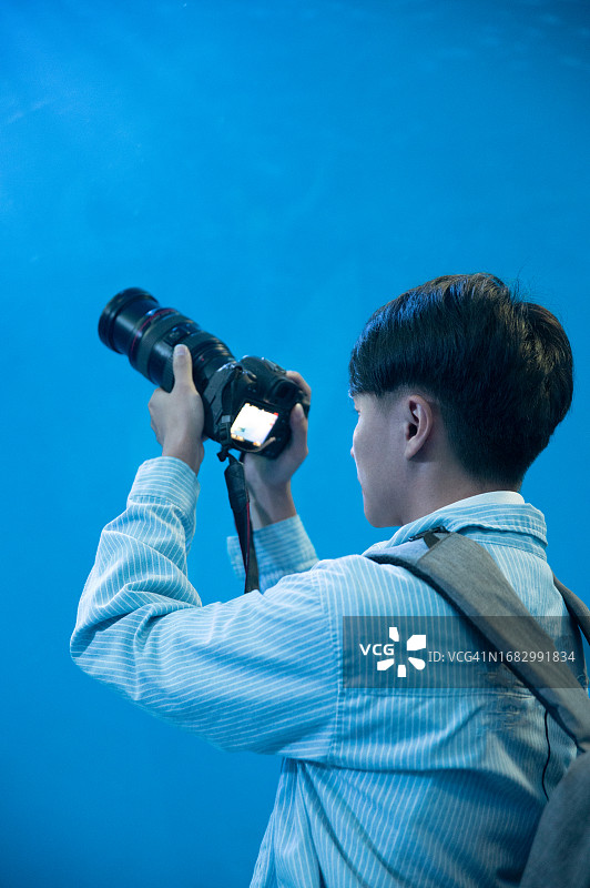 男背包客在水族馆里用相机拍摄海洋生物图片素材
