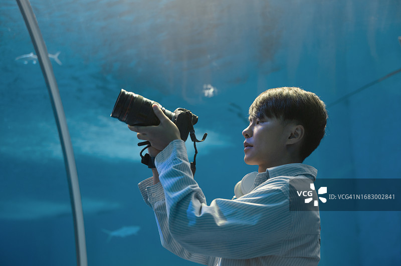 男背包客在水族馆里用相机拍摄海洋生物图片素材