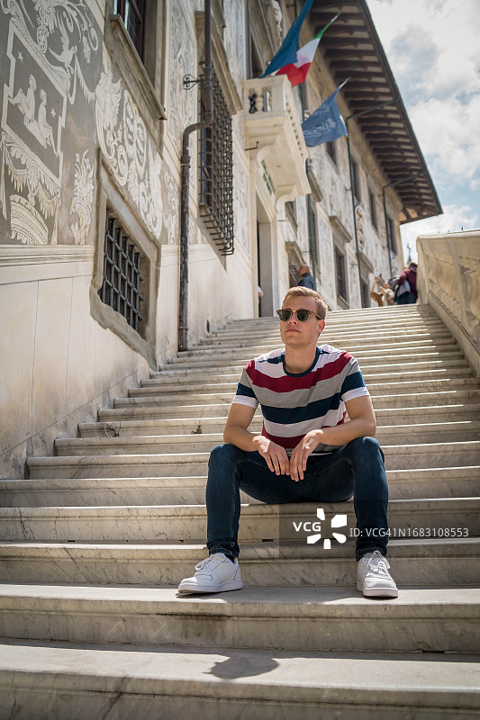 在意大利佛罗伦萨，年轻男子坐在阿诺河边欣赏风景的肖像图片素材
