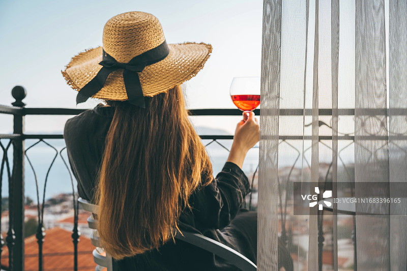 戴着柳条帽，在私人别墅阳台上喝玫瑰酒的女人图片素材