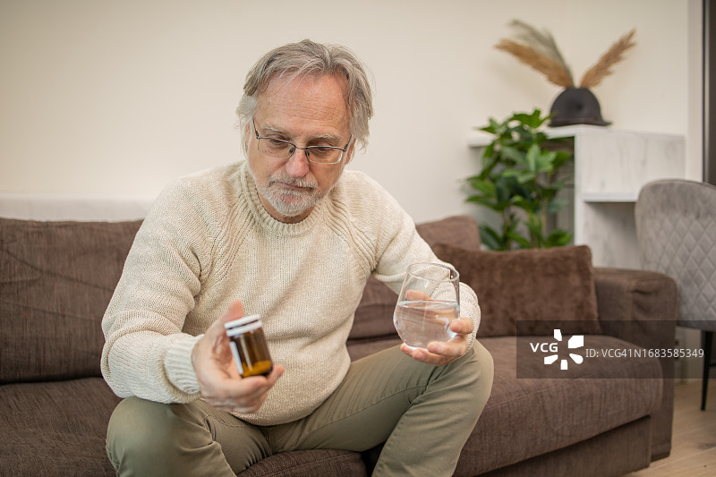 年长的男人坐在客厅的沙发上吃药图片素材