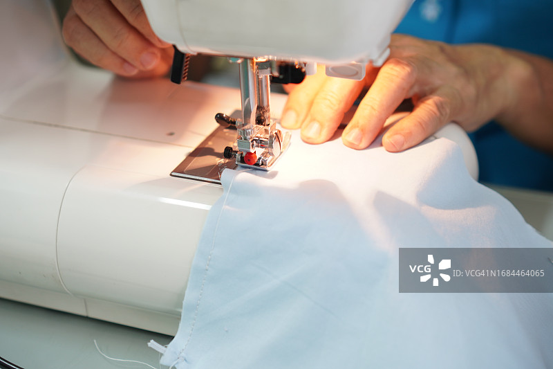 女人的手在缝纫机上操作配件设备，白色织物特写图片素材