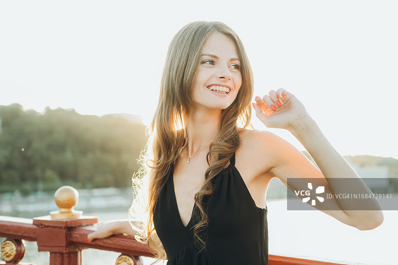 身穿黑色连衣裙的年轻女子站在户外木制栏杆旁图片素材